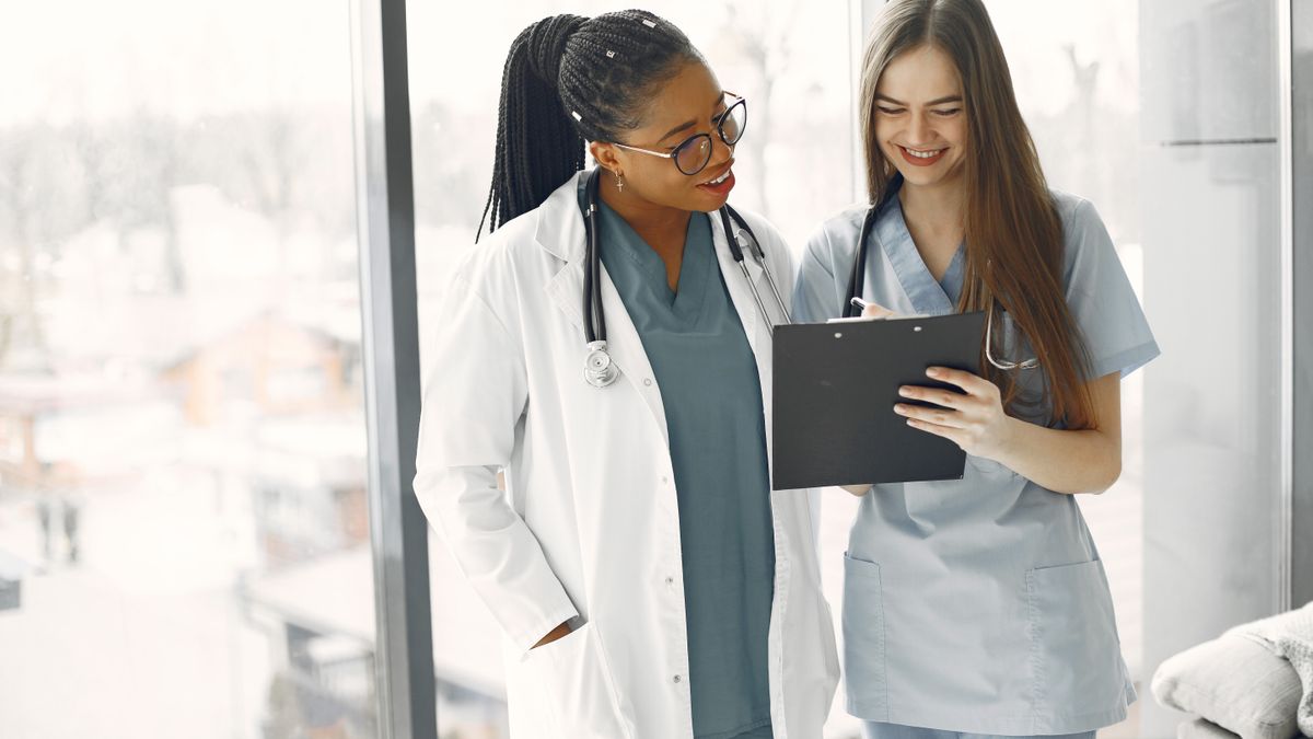 An experienced clinician mentoring a new healthcare hire with a clipboard